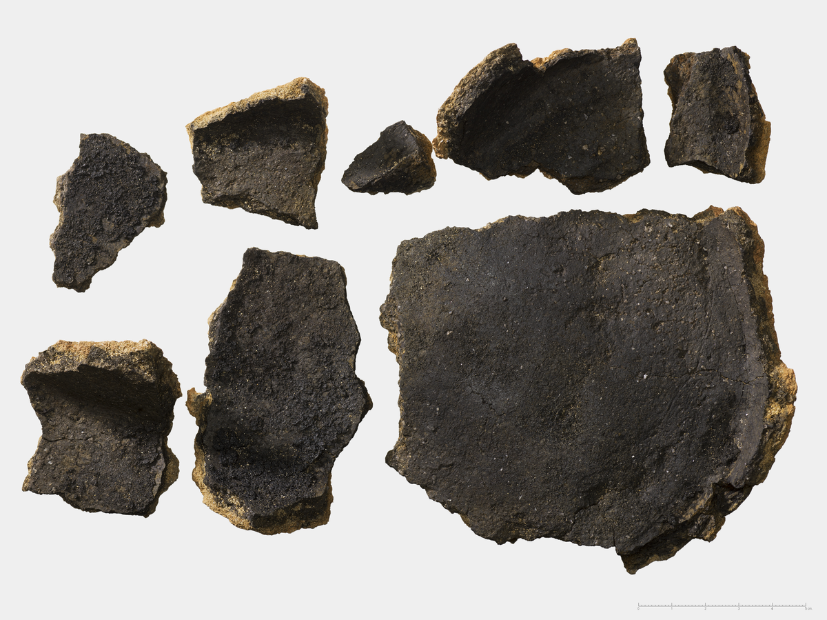 8 Skår av vanlig brukskeramikk. Grov-magret leire. Rødbrun farget utside, svartgrå innside. Alle skårene hører til det samme karet og de utgjør nesten hele bunnen av et kar. Skårene passer sammen og kan limes. Deler av karets kropp er bevart langs sidene av karet. De danner her en ca. 70-80 graders vinkel, og karet er nok buet/avrundet. Karet er ca. 0.5cm tykkere der hvor veggen vinkler utover. Det er matskorpe langs hele karets innside. Karet er grovt polert. Trolig kar til oppbevaring/matlaging. Største mål: Tykkelse: 0,7 cm. Lengde: 11.5 cm. Bredde: 11 cm. Funnet i ovnen AO2478. 2 Kar er tatt på samme S-NR. Merk at dette er feil, de to karene på samme S-NR hører ikke sammen.
