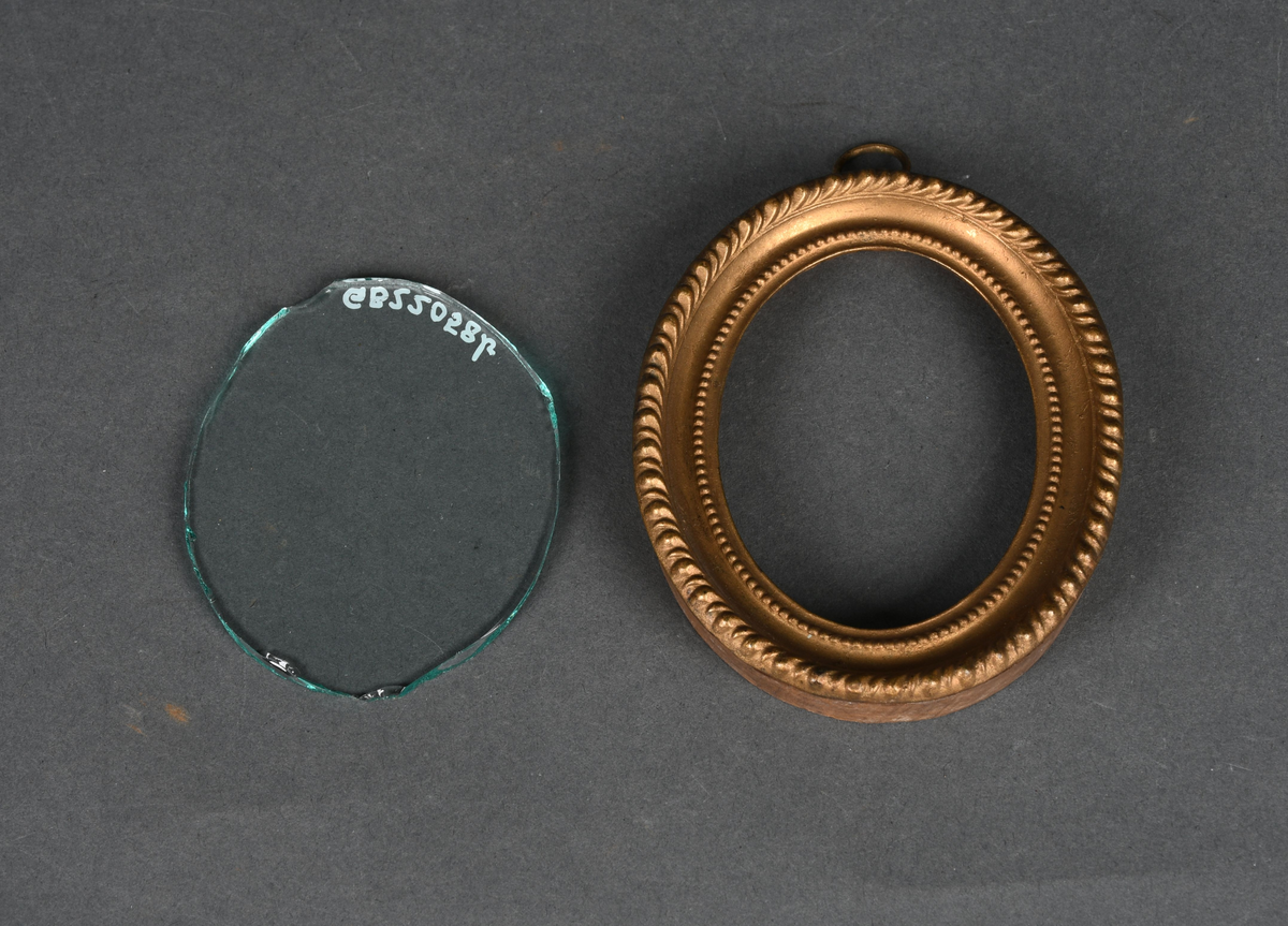 Oval bilderamme med treramme og gullmalt, profilert metallkant med to perlerader. Rammen har et løst, beskyttende glass og en ring festet til øvre kant.