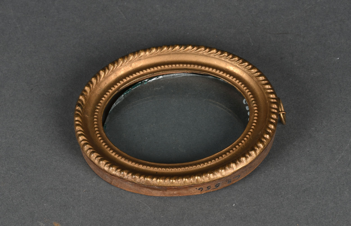 Oval bilderamme med treramme og gullmalt, profilert metallkant med to perlerader. Rammen har et løst, beskyttende glass og en ring festet til øvre kant.