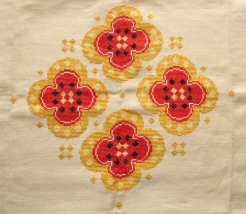 Broderad kvadratisk stor duk. Korsstygn på halvblekt linne med lingarn i rött, gult, svart, ljusgult och vitt.
 Mönstret: Fyra stora vallmoblommor med små prickar emellan placerade på dukens mitt. En röd och en gul rand längs fållarna.