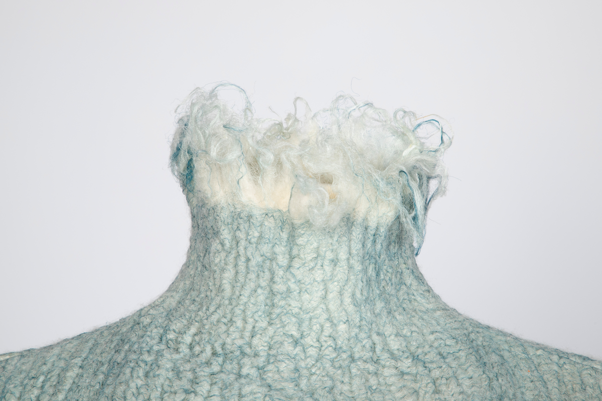 Kjole og overdel i tovet lys turkis-blå-grå ull og silkeorgansa med innslag av metalltråd. Benhvitt underskjørt av silkeorganza med metallstreng i nederkant.