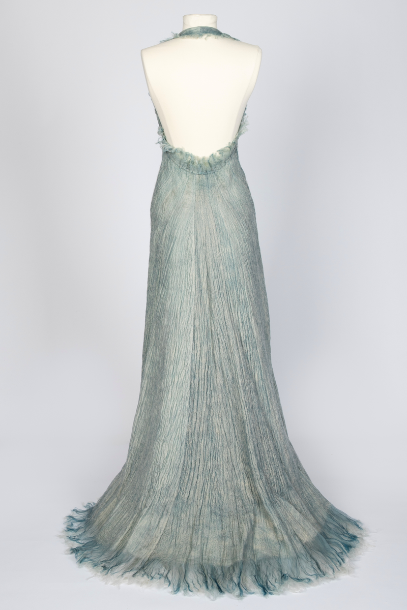 Kjole og overdel i tovet lys turkis-blå-grå ull og silkeorgansa med innslag av metalltråd. Benhvitt underskjørt av silkeorganza med metallstreng i nederkant.