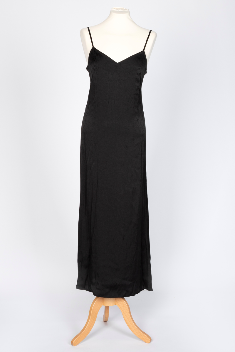 Fotsid kjole med tilhørende liten hatt. Kjolen består av en svart underkjole i silke med v-formet utringning og smale skulderstropper og en overkjole av gjennomsiktig, mønstertrykt tyllstoff med blonder. Mønsteret består av svarte, brune, beige, hvite og rosa sirkler. Rund utringning og korte, volangeformede ermer. Kjolen har påsydde paljetter og Chanels monogram i matchende farger. Tilhørende liten silkechiffonhatt i solhattfasong, påtrykt samme mønster som kjolen.