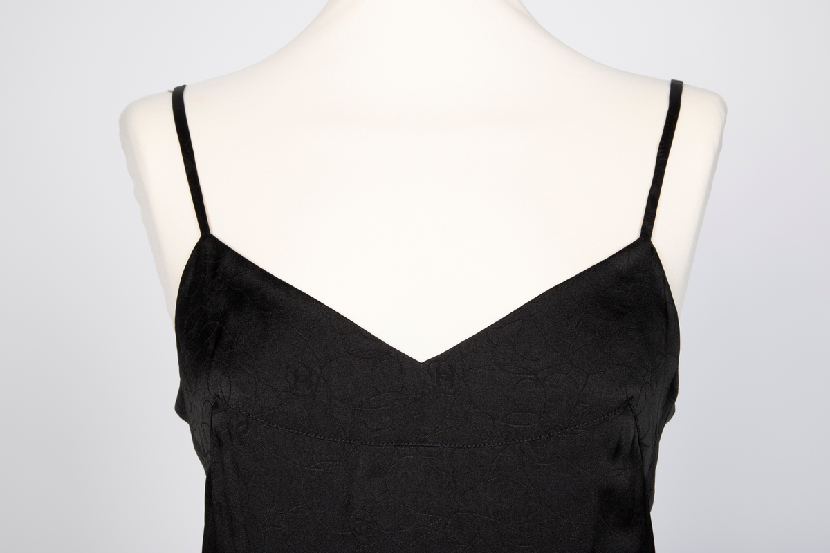 Fotsid kjole med tilhørende liten hatt. Kjolen består av en svart underkjole i silke med v-formet utringning og smale skulderstropper og en overkjole av gjennomsiktig, mønstertrykt tyllstoff med blonder. Mønsteret består av svarte, brune, beige, hvite og rosa sirkler. Rund utringning og korte, volangeformede ermer. Kjolen har påsydde paljetter og Chanels monogram i matchende farger. Tilhørende liten silkechiffonhatt i solhattfasong, påtrykt samme mønster som kjolen.