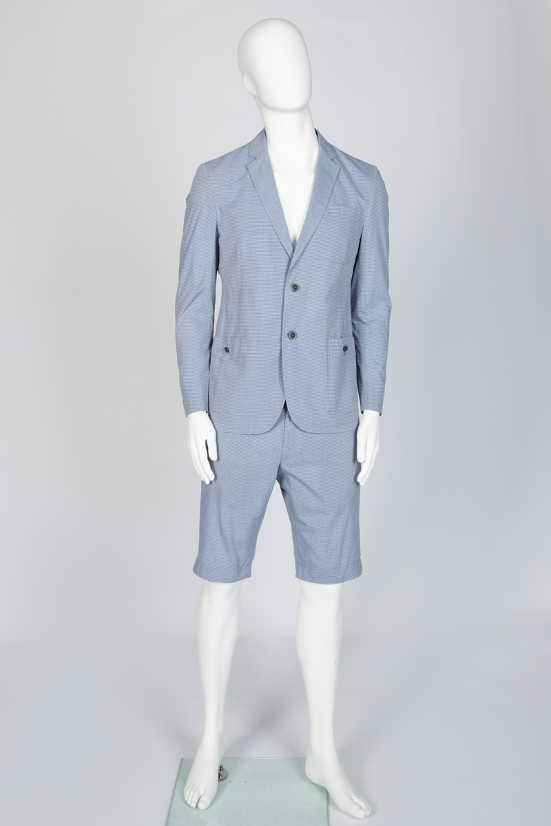 Herredress i smårutete, lyseblått og hvitt bomullsstoff bestående av kortbukse og jakke. Jakken er enkeltspent, med to knapper, har smale slag og krage og avrundede forbredder. Utenpåsatte lommer med nedstukket "klaff" i spiss med knapphull og knapp. Brystlomme. Ermene har åpen sliss med tre knapphull og knapper. Splitt midt bak. Fôr i ermer og nakken, samt to innvendige brystlommer lukket med knapp. Buksen er lårkort, har to stikklommer, en urlomme på venstre side og to baklommer med klaff. Linning med sju beltehemper, midt bak og over urlommen er det dobbel beltehempe. Gylf med glidelås og metallhektelukning i linningen.