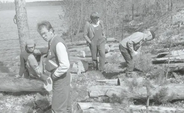 fire personer studerer tømmeret til naustet som ligger spredt rundt på bakken på blokkodden. TØmmeret ligger ved vannkanten til Drevsjøen og rundt ser vi skog. 