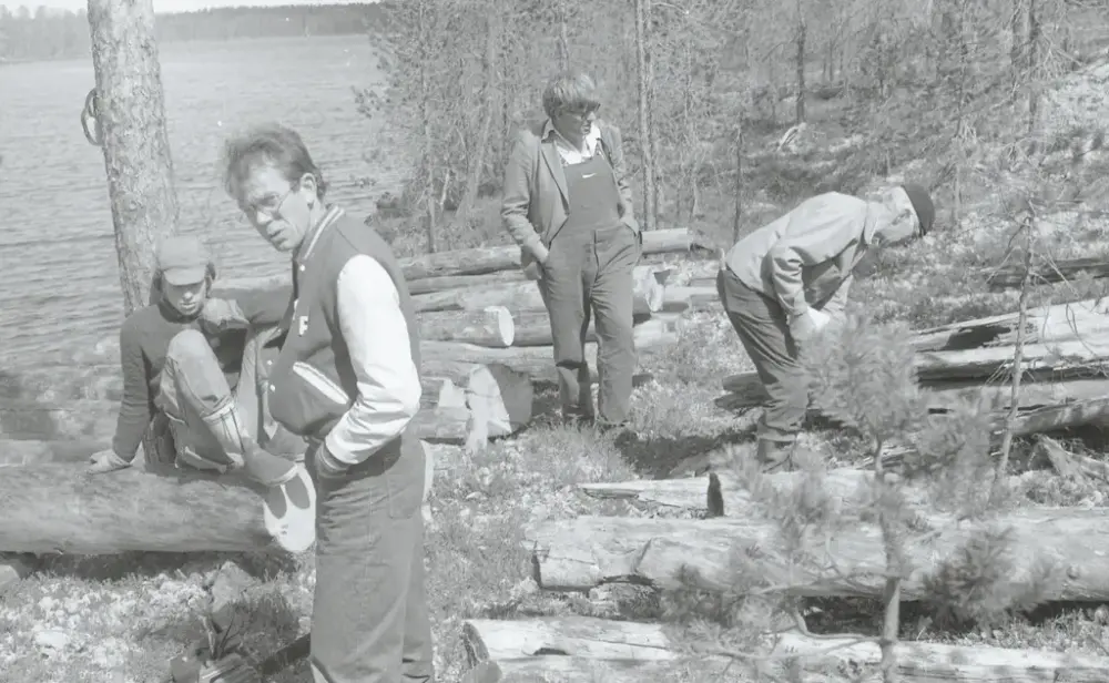 fire personer studerer tømmeret til naustet som ligger spredt rundt på bakken på blokkodden. TØmmeret ligger ved vannkanten til Drevsjøen og rundt ser vi skog. 