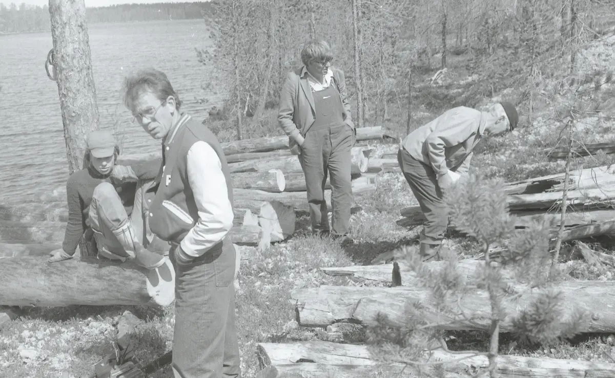 fire personer studerer tømmeret til naustet som ligger spredt rundt på bakken på blokkodden. TØmmeret ligger ved vannkanten til Drevsjøen og rundt ser vi skog. 