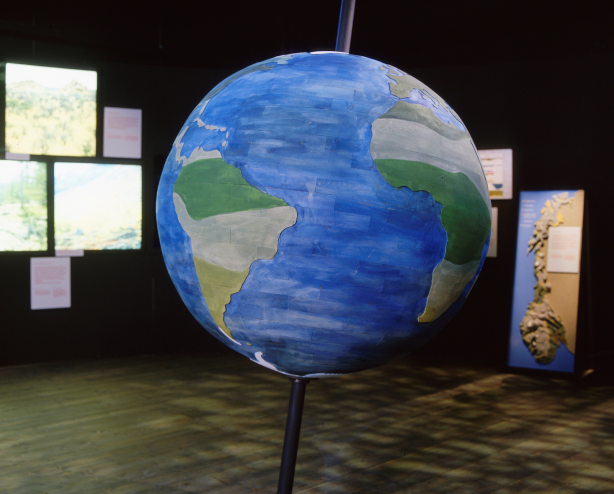 Treglobus med cirka 1 meters diameter, montert på en skrå akse i introduksjonsrommet til basisutstillingen «Tid for Skog» på Norsk skogmuseum, bygd vinteren 2000-2001. Tanken med globusen var at den skulle minne publikum om at en stor del av kloden (cirka 70 prosent) er dekket av vann, og at landarealene har ulike klimasoner, som disponerer for ulike typer skog. Cirka 28 prosent av landarealet på kloden er skogdekt, men trærne utgjør 82 prosent av den terrestriske biomassen. Som en referanse til det skoglige mangfoldet på kloden ble det montert fotografier fra fem ulike skogstyper på en vegg i det samme rommet, men denne veggen er ikke synlig på dette bildet. I stedet ser vi (helt til høyre) ett av fire relieffkart over Norge, som illustrerer den norske skogens innvandringhistorie i fire faser – med endepunkt i et idealisert pollendiagram for norske skogstrær. Rommet disse montasjene befinner seg i har følgende introduksjonstekst: 

«I barskogens land
Vi bor på taigaen. Sammen med mennesker i Kanada, Alaska, Russland, Finland og Sverige. Du kan ferdes jorda rundt langs de 60:e og 70:e breddegrader og heler tida befinne deg i den samme skogen. Barskogen er ung, fordi innlandsisen dekket våre områder til for ca. 10 000 år siden. Mennesket har over tid utnyttet skogen til ulike formål. Skogen kan også bli rammet av skader av forskjellige slag. Nå diskuteres det mye om hvorvidt mennesket er i ferd med å forandre verdens klima gjennom utslipp og forurensninger.»