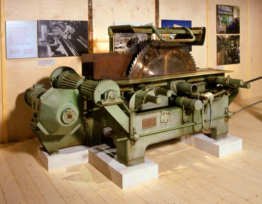 Grønnlakkert sirkelsag med to blader, montert i rommet «Over hele verden» i Norsk skogmuseums basisutstilling «Tid for Skog», som ble bygd vinteren 2000-2001. Tematikken i rommet, som ble prosjektert av daværende førstekonservator Magne Rugsveen, er industriell bearbeiding av norsk tømmer med tanke på salg, både innenlands og på utenlandske markeder. Mesteparten av rommet dreier seg om treforedlingsindustrien, som ved å slipe treet eller hogge det til flis og koke den i kjemikalier, har produsert kartong og papir. Den norske treforedlingsindustriens trekjemiske produkter vises også. Trelastnæringa, som bearbeider tømmeret til konstruksjonsvirke, er viet mindre oppmerksomhet, bare denne saga og en flott modell av ei lokomobilsag. Trelast- eller skurlastproduksjonen er imidlertid tema også i et annet utstillingsrom – «Skogen som gullgruve» – der det blant annet står en modell av ei oppgangssag, og hvor det er fokus på  at trelast var en eksportartikkel som svært tidlig ble viktig for Norge.

«Gullhøna» ble utviklet av firmaet J. A. Jensen og Dahl (JAJOD) like før 2. verdenskrig, og denne sagtypen ble polulær på mellomstore sagbruk i Norge de første to-tre tiåra etter krigen. Gullhøna hadde to sirkelsagblader som lett lot seg regulere, slik at avstanden mellom bladene gav den best mulige utnyttinga av stokken ble optimal. Den saga vi ser på fotografiet er om lag 3,2 meter lang, snaut 2 meter bred og 1,35 meter høy. Diameteren på sagbladene er om lag 1 meter. Saga inngår i en montasje som har denne teksten:

«Lokal sagbruksdrift
Mot slutten av 1930-tallet var importen av trelast større enn eksporten. Myndighetene så på lokal sagbruksdrift som et mottiltak mot den økonomiske depresjonen. Etter 1945 var det svært mange sagbruk i Norge, nærmere 8 000 anlegg. Omtrent halvparten var gardssager. I Hedmark var det 321 sagbruk i regulær drift med et årlig tømmerbehov på rundt 550 000 kubikkmeter. Rundt 1950 hadde norske sagbruk lav teknisk standard, men ny teknologi ble tatt i bruk. Jajod med produksjon i Lillehammer, var en viktig bedrift for fornyelse av næringa. «Gullhøna» var en viktig saginnretning i Jajods teknologi.»