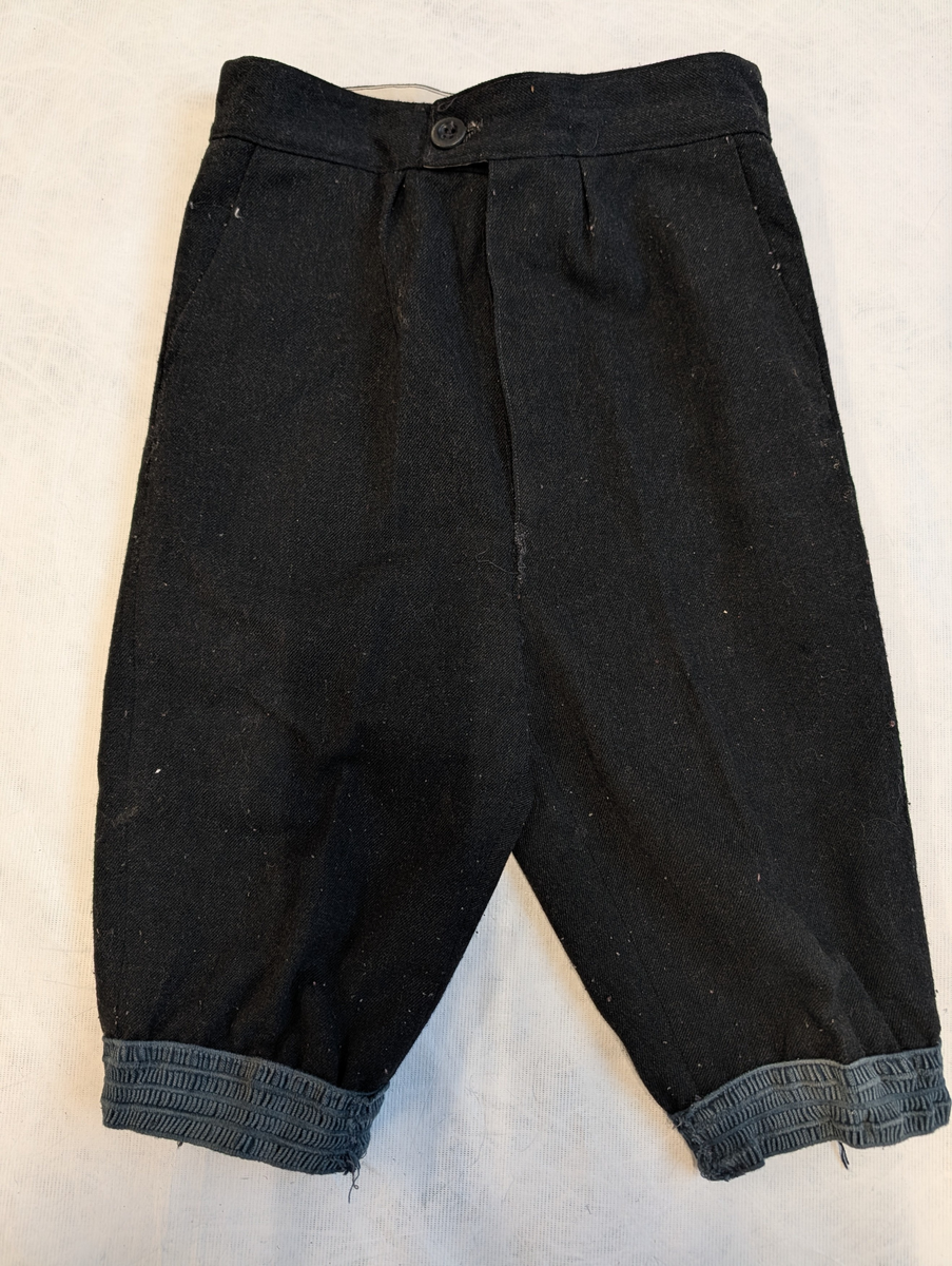 Nikkers er sydd i vanlig buksemønster med lommer i sidene og gylf foran som kneppes med to knapper. Buksen kneppes i livet med knapp og knapphull. Ved kneet rynkes buksen sammen med en bred strikk.