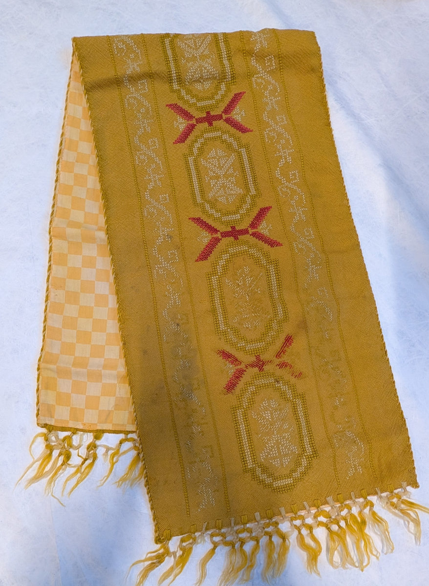 Teppet er brodert med tre felter midt på, én bred bord og to smale på hver side. Snorer er sydd fast i kanten langs sidene, og det har frynser med fint knyttede avslutninger i hver ende. Langs kanten går geometriske, lignende border.