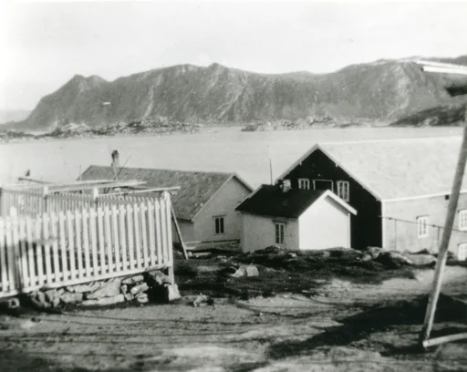 Gjesvær. Deler av bebyggelsen og et gjerde på en liten steinmur på venstre side.