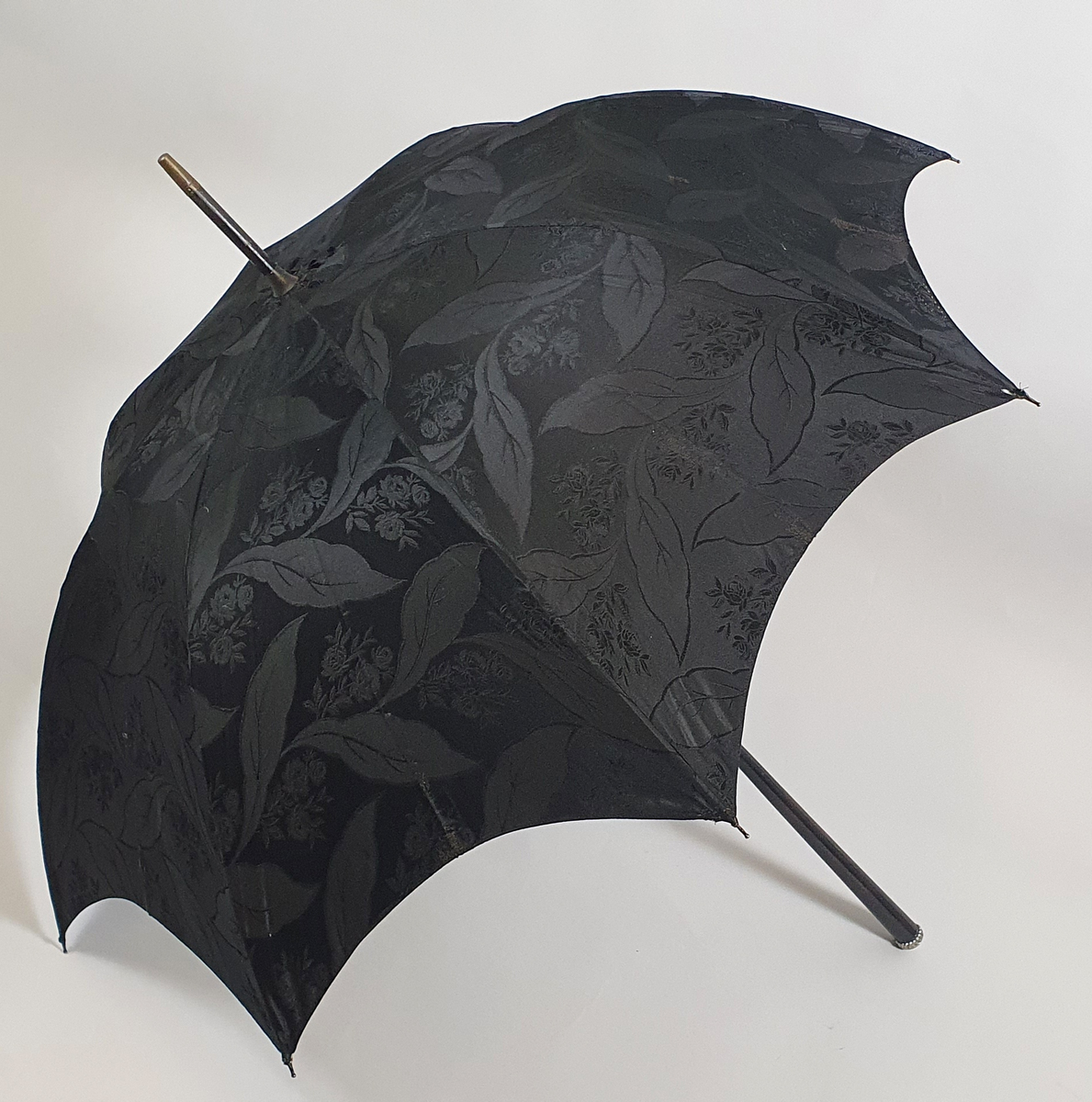 Dameparaply med sort silketrekk, metallspiler, trestang og på enden av håndtaket en liten metallholk.