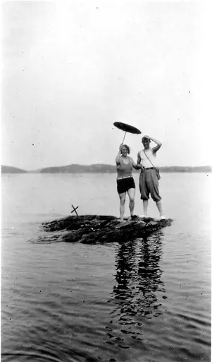 To personer på et lite skjær. Iført badetøy og parasoll