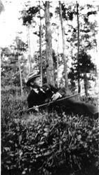 Mann med hatt og stokk slapper av i et skogbryn