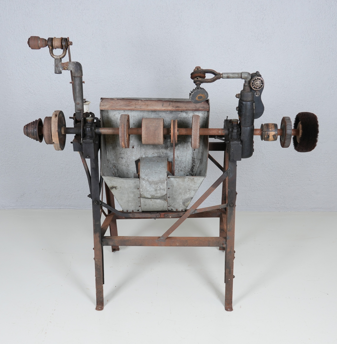 Pussemaskin for sko. Underdel i metall (4 bein). Oppå underdelen er det montert anordning i hardt tre og metall, mellom anna ein aksling i metall. Sandpapir og kostar er feste på sirkelforma delar, som er feste inn på akslingen. Under delane med sandpapir er det montert ei oppsamlingsanordning i blikk. Denne har opning ut på andre sida.