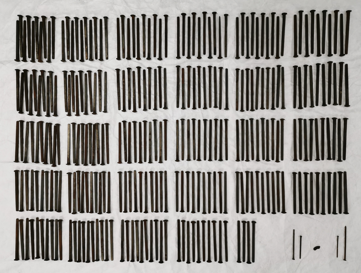 Trekasse fylt med 284 store spikar. På kassa er det trykt tekst. Oppsida av kassa er halvt ope, slik at øvre halvdelen av spikrane er synlege. Spikrane er like: Hovudet meir ovalt enn rundt, og litt kantete. Sjølve spikaren har fire sider og smalnar inn nedst. To av sidane er breiare enn dei to andre.