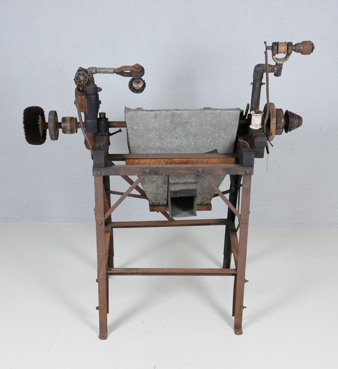 Pussemaskin for sko. Underdel i metall (4 bein). Oppå underdelen er det montert anordning i hardt tre og metall, mellom anna ein aksling i metall. Sandpapir og kostar er feste på sirkelforma delar, som er feste inn på akslingen. Under delane med sandpapir er det montert ei oppsamlingsanordning i blikk. Denne har opning ut på andre sida.