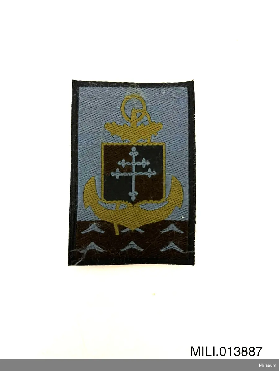 Tilläggstecken av textil med maskinvävt motiv. Med kardborrefästning på baksidan.