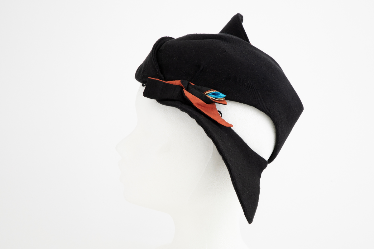 Asymmetrisk hatt i svart ull- og silkeblanding, rustrød råsilke og polyesterbånd på innsiden.