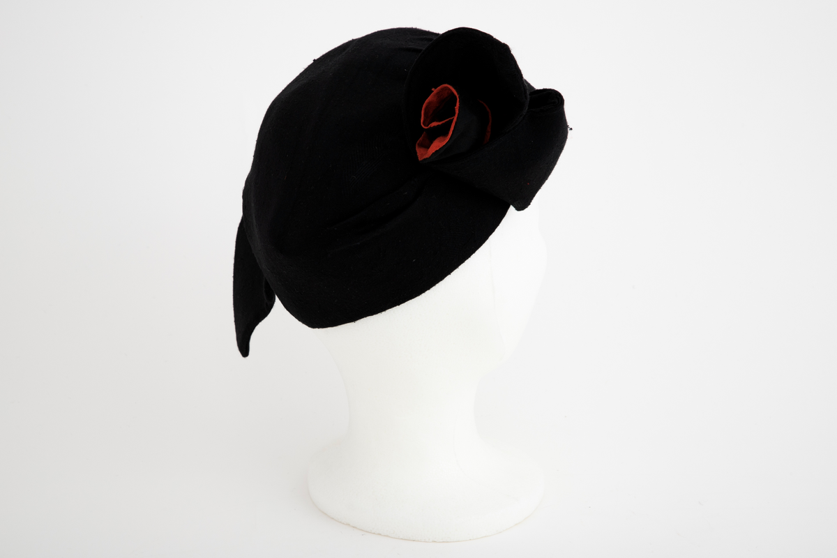 Asymmetrisk hatt i svart ull- og silkeblanding, rustrød råsilke og polyesterbånd på innsiden.