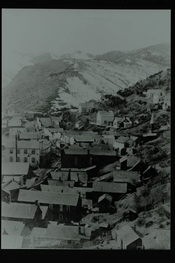 Et tettsted med flere bygninger i en dal. Åsside til høyre og fjell bak. Høyre halvpart av et større landskapsbilde.