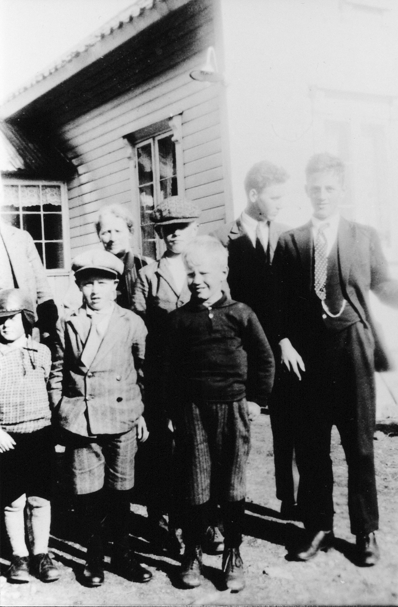 En gruppe mennesker foran et hus med lys, horisontal kledning. 