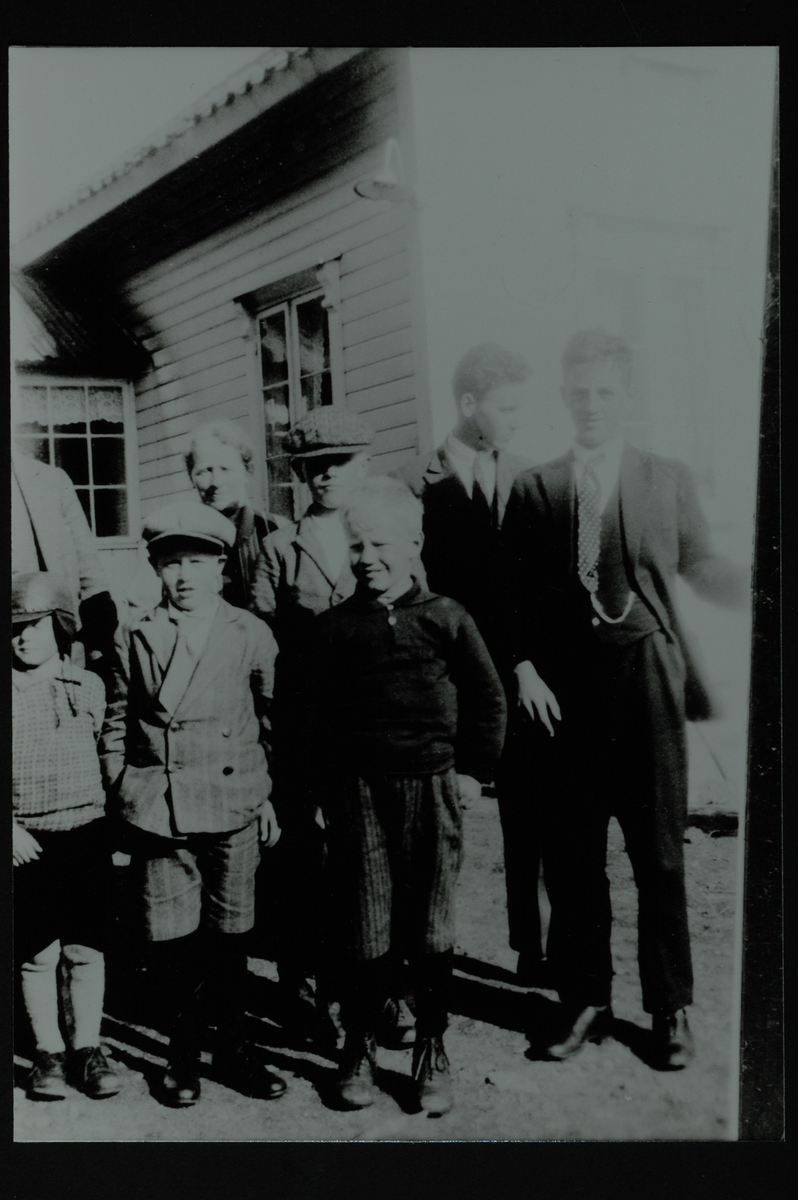 En gruppe mennesker foran et hus med lys, horisontal kledning. 