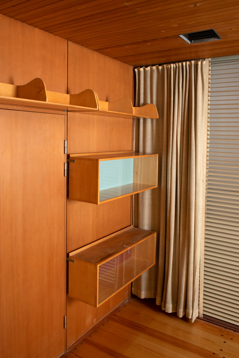 Panelvegg med flyttbare hylleseksjoner. Blant seksjonene finnes to diskmontre i mørkebrun rio-palisander med glass i lokket. Toppflatene skrån fremover, og lokkene er låsbare. Festet til bakvegg. Det er fire åpne reoler i dansk løn. Disse er to-det i bredden med lave skillevegger med buet profil. Det er fire lukkede veggmontre i dansk lønn. Glass på forsiden. Rektangulær kasseform. I tre av skapene er bakveggen malt lys blå, i den fjerde er bakveggen rødbrun. Bakveggen og dend rør er i douglas-gran