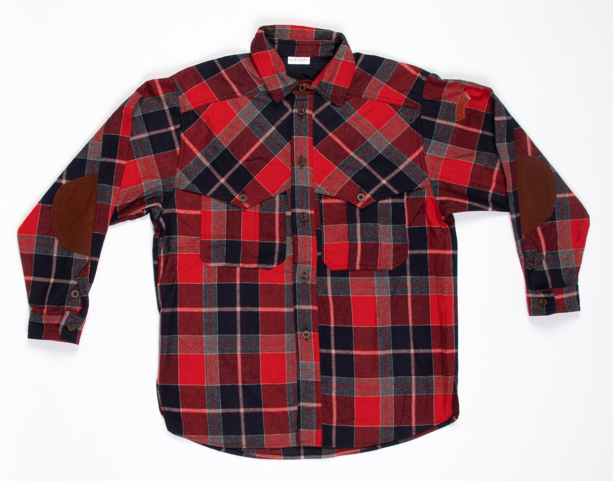 Rutete skjorte i ullblanding. Søm i hver side, litt oppsplittet nederst. Åpen foran med stolpe, knappet med seks knapphull og knapper. Dobbelt krage med små spisser og med brunt reinskinn på linningens utside. Bærestykke over skuldrene. En stor lomme på hvert forstykke. Et ekstra forstykke fra bærestykket foran danner klaffer med knapping for lommen. Skjorten er lett avrundet nedentil. Isydde ermer med mansjett og knapping. På albuene en skinnlapp og på venstre erme påsydd skinnlapp, hvorpå SONDRE.