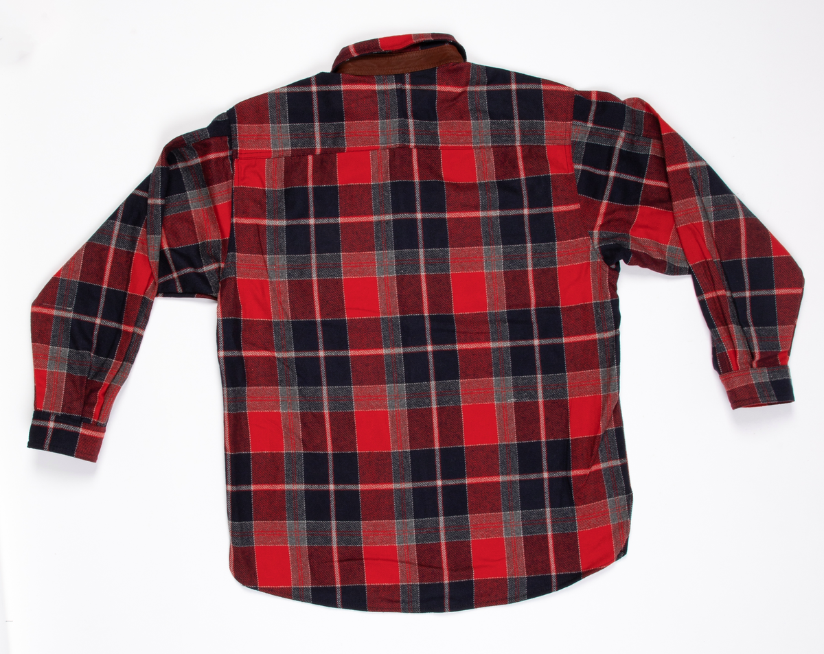 Rutete skjorte i ullblanding. Søm i hver side, litt oppsplittet nederst. Åpen foran med stolpe, knappet med seks knapphull og knapper. Dobbelt krage med små spisser og med brunt reinskinn på linningens utside. Bærestykke over skuldrene. En stor lomme på hvert forstykke. Et ekstra forstykke fra bærestykket foran danner klaffer med knapping for lommen. Skjorten er lett avrundet nedentil. Isydde ermer med mansjett og knapping. På albuene en skinnlapp og på venstre erme påsydd skinnlapp, hvorpå SONDRE.