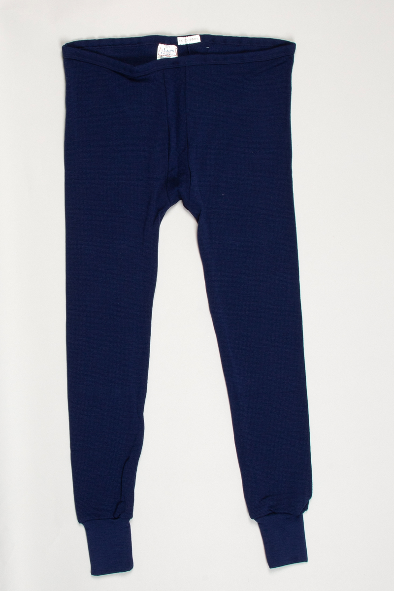 Longs i mønsterstrikket mørkeblått ullgarn. Strikk i livet. To sømmer midt foran og bak på livet til skrittet. Lange ben, trange ved ankelen med påsydd dobbelt glattstrikk. En søm på innsiden av hvert ben.