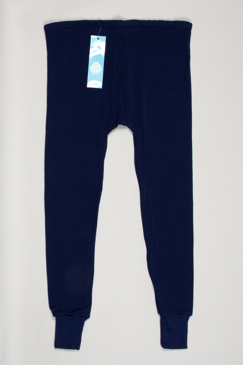 Longs i mønsterstrikket mørkeblått ullgarn. Strikk i livet. To sømmer midt foran og bak på livet til skrittet. Lange ben, trange ved ankelen med påsydd dobbelt glattstrikk. En søm på innsiden av hvert ben.