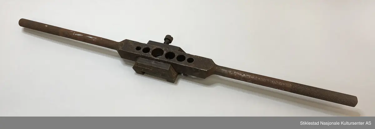 Svingjern med 6 hull, påmontert en kloss med stråstilte sider, stort hull i midten. Merket med Ø fire steder.