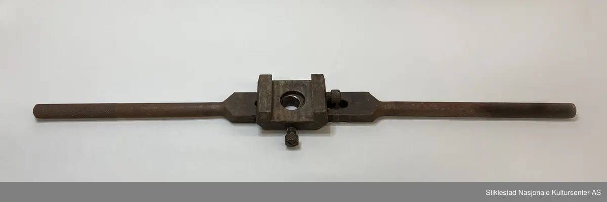 Svingjern med 6 hull, påmontert en kloss med stråstilte sider, stort hull i midten. Merket med Ø fire steder.