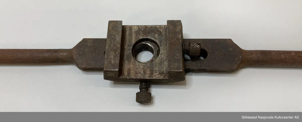 Svingjern med 6 hull, påmontert en kloss med stråstilte sider, stort hull i midten. Merket med Ø fire steder.