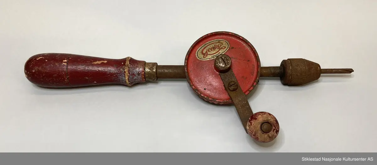 Fabrikkprodusert drill/hånddrill med rødfarget treskaft, sveiv og tannhjul. Ellers jern/metall. Det står en kort bor i chuck (kjoks). Merket 301/1 Germany på tannhjul/drivhjul. Andre siden et merke i gullfarge med rød skrift: Genko, Germany.
