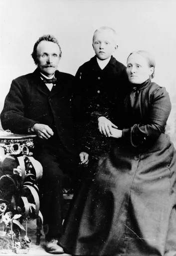 Portrett av en mann, en kvinne og en gutt. De voksne sitter, barnet står bak og mellom dem. Mannen lener sin høyre arm på et lite bord.