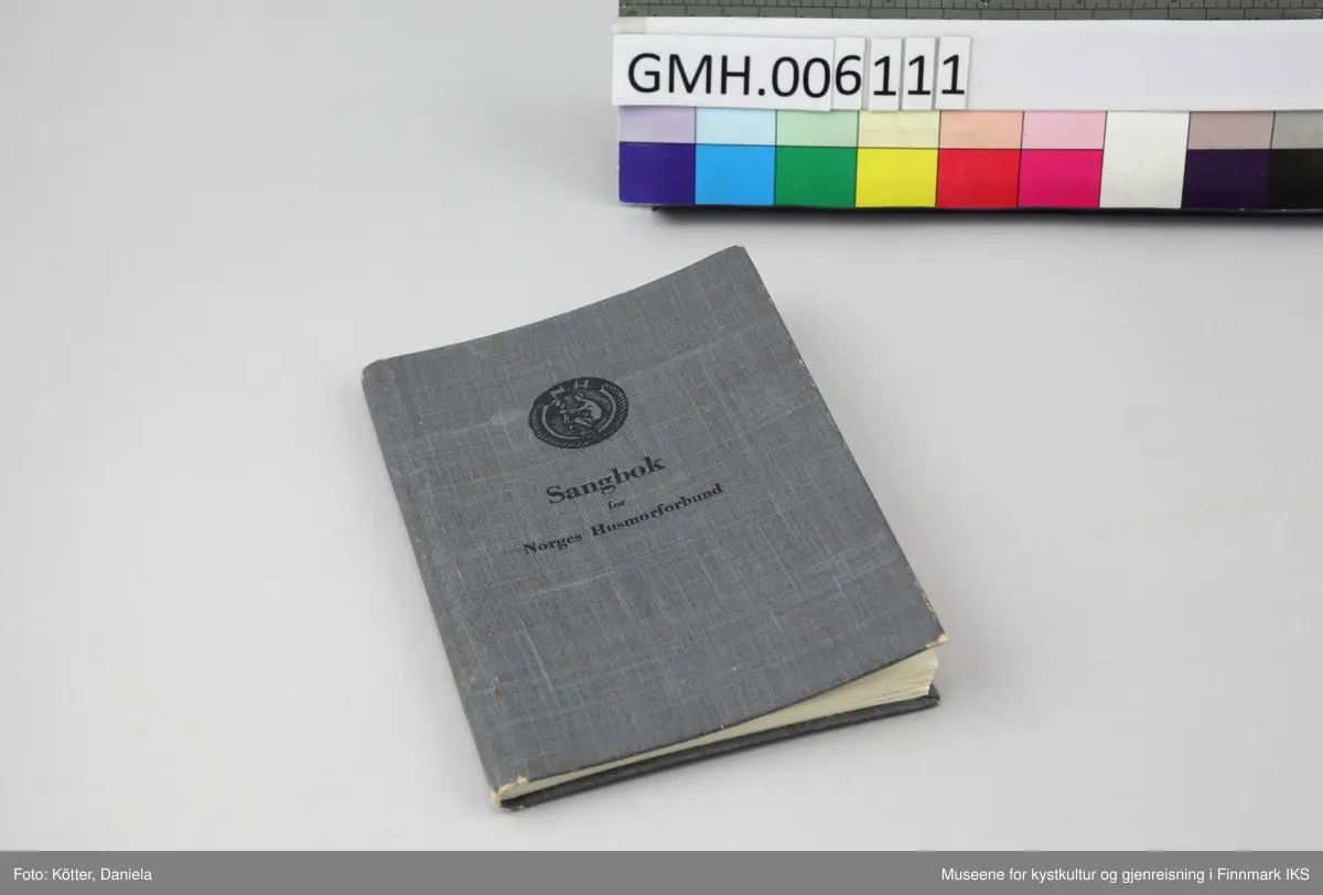 Sangboken har omslag av papp som er trukket med mørkt gråblått, lettmønstret papir. Tittelen, Husmorforbundets runde symbol, bokstavene "N.H." samt en kvinne som huker seg ned og legger hendene sine på et barns armer, er trykket med lett innpregning på omslagets forside i svart. Noen sider har brett på hjørnene. Omslaget er lett bøyd utover. Papirsidene er delvis gulnet. Boka er utført med trådbinding.