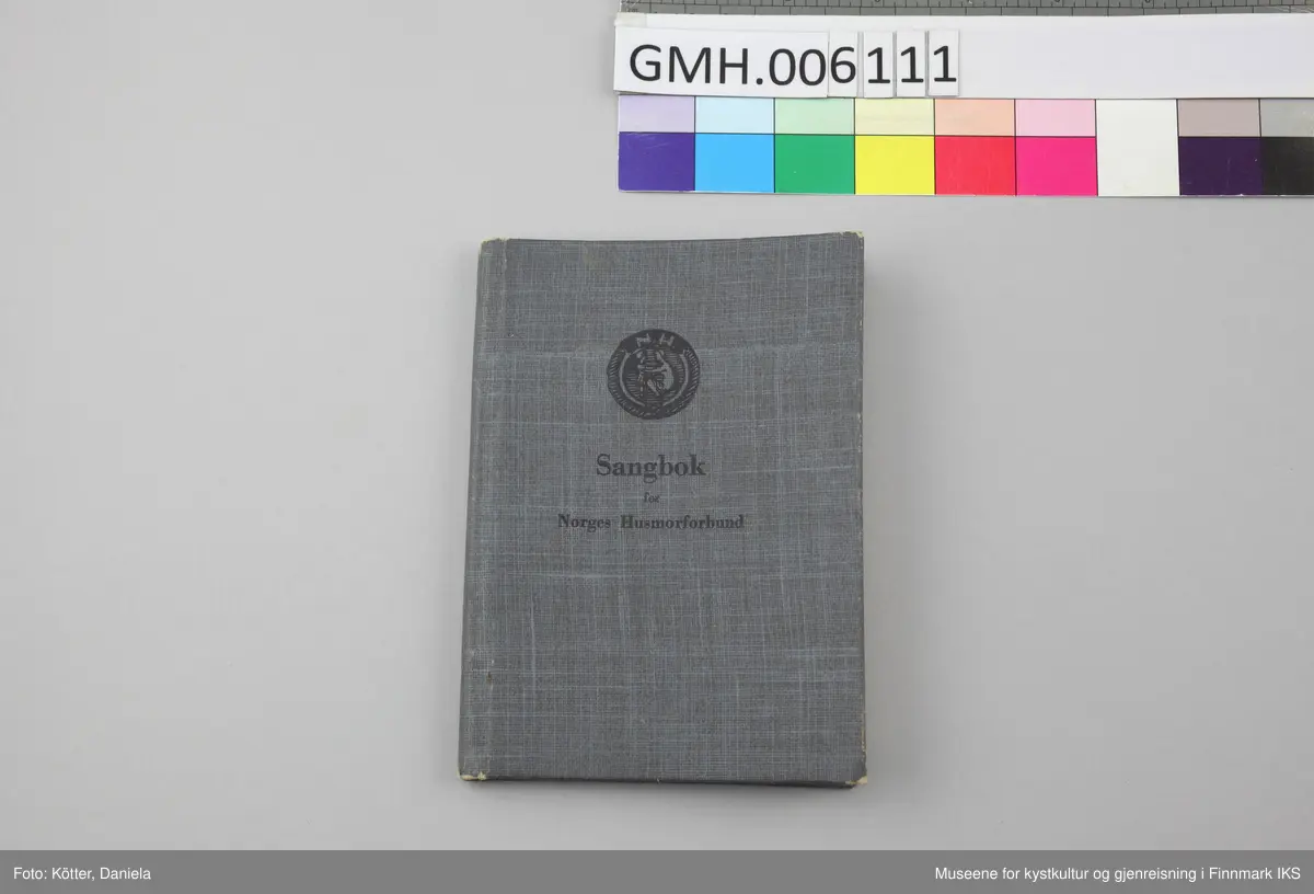 Sangboken har omslag av papp som er trukket med mørkt gråblått, lettmønstret papir. Tittelen, Husmorforbundets runde symbol, bokstavene "N.H." samt en kvinne som huker seg ned og legger hendene sine på et barns armer, er trykket med lett innpregning på omslagets forside i svart. Noen sider har brett på hjørnene. Omslaget er lett bøyd utover. Papirsidene er delvis gulnet. Boka er utført med trådbinding.