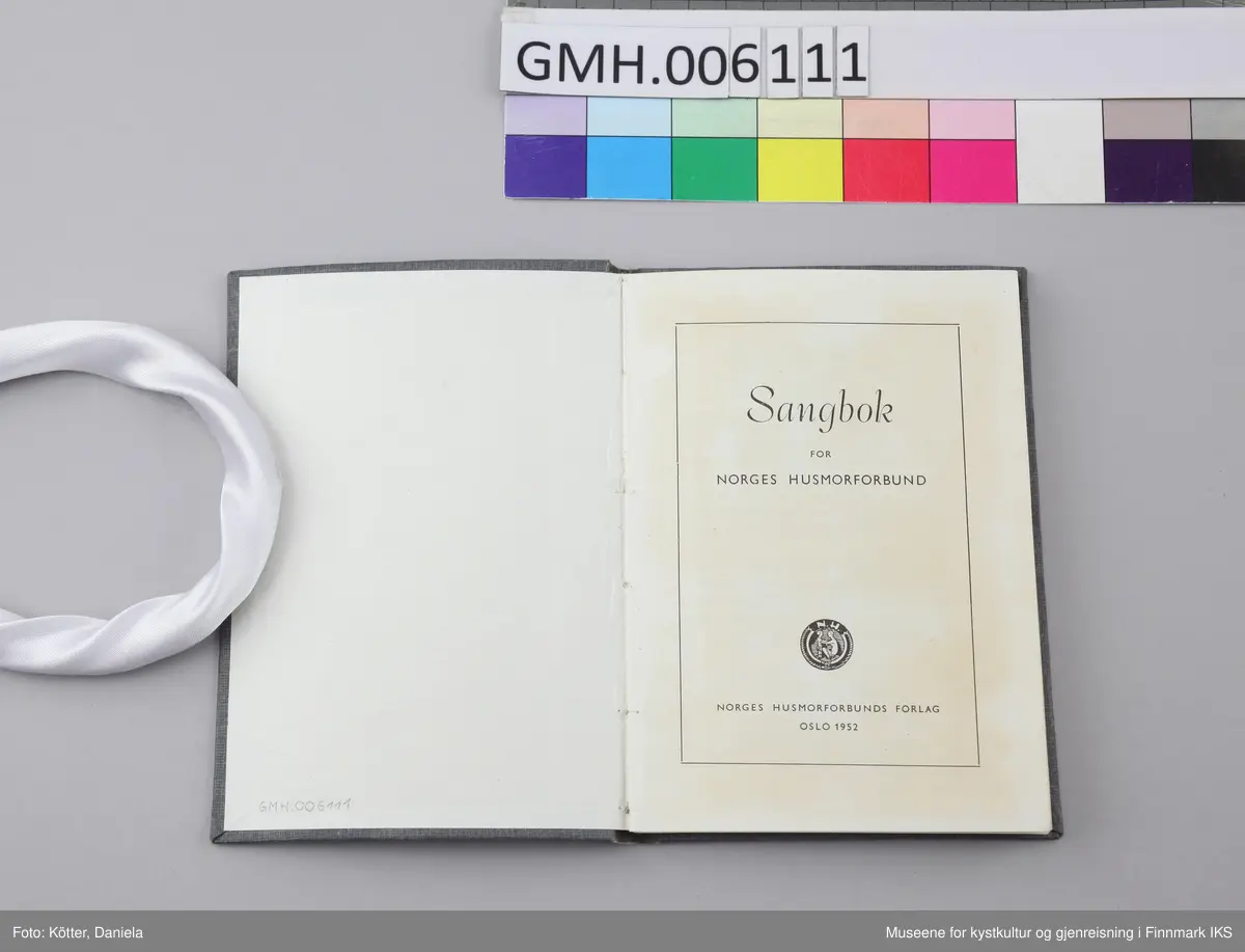 Sangboken har omslag av papp som er trukket med mørkt gråblått, lettmønstret papir. Tittelen, Husmorforbundets runde symbol, bokstavene "N.H." samt en kvinne som huker seg ned og legger hendene sine på et barns armer, er trykket med lett innpregning på omslagets forside i svart. Noen sider har brett på hjørnene. Omslaget er lett bøyd utover. Papirsidene er delvis gulnet. Boka er utført med trådbinding.