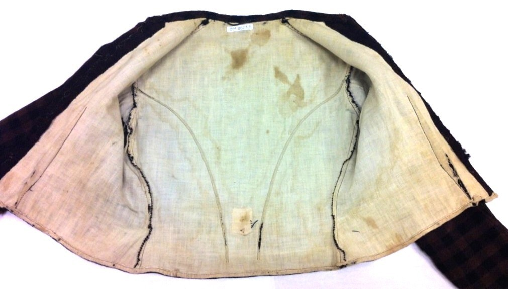 Kjoleliv i svart og brunrutet ull i hjemmevevd toskaft med ermer og bol i samme stoff. Livet er i dag velbrukt, falmet og slitt, med hull på albuene. Sydd for maskin og hånd med panelsøm og bakovertrekte skuldersømmer og sidesømmer. Rund rigning i halsen og buet fremkant. 1,5 cm bred halslinning sydd med maskin og lagt over og festet med faldesting og prikkesting i svart bomullstråd. Tett lukket med 13 par metallhekter med en 1,5 cm bred stolpe som skjuler hektingen. Kantene fremme er først sydd med maskin med brun sytråd og med leggsøm med brun bomullstråd. Livet har et innsnitt som er 3 cm på det bredeste under bysten, sydd med maskin. Smal tosøms krokarm. Livet er helfôret med ubleket bomull i hjemmevevd toskaft og sydd på samtidig som ullstoffet ble sydd sammen med maskin og spilesøm med tykk bomullstråd for hånd. Livet brukes ned i stakken og har hatt en metallkrok midt på bak til å hekte stakken på.