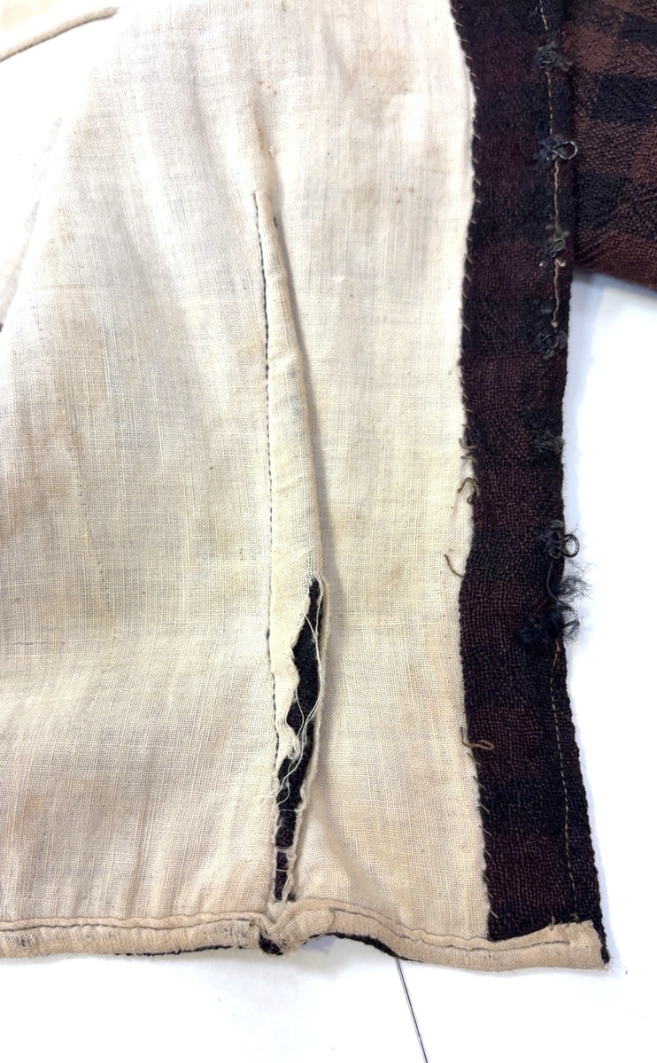 Kjoleliv i svart og brunrutet ull i hjemmevevd toskaft med ermer og bol i samme stoff. Livet er i dag velbrukt, falmet og slitt, med hull på albuene. Sydd for maskin og hånd med panelsøm og bakovertrekte skuldersømmer og sidesømmer. Rund rigning i halsen og buet fremkant. 1,5 cm bred halslinning sydd med maskin og lagt over og festet med faldesting og prikkesting i svart bomullstråd. Tett lukket med 13 par metallhekter med en 1,5 cm bred stolpe som skjuler hektingen. Kantene fremme er først sydd med maskin med brun sytråd og med leggsøm med brun bomullstråd. Livet har et innsnitt som er 3 cm på det bredeste under bysten, sydd med maskin. Smal tosøms krokarm. Livet er helfôret med ubleket bomull i hjemmevevd toskaft og sydd på samtidig som ullstoffet ble sydd sammen med maskin og spilesøm med tykk bomullstråd for hånd. Livet brukes ned i stakken og har hatt en metallkrok midt på bak til å hekte stakken på.