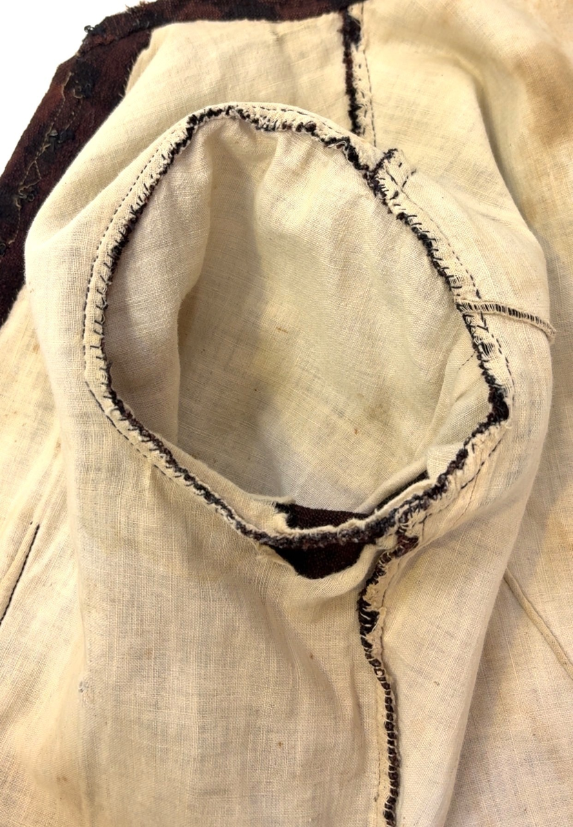 Kjoleliv i svart og brunrutet ull i hjemmevevd toskaft med ermer og bol i samme stoff. Livet er i dag velbrukt, falmet og slitt, med hull på albuene. Sydd for maskin og hånd med panelsøm og bakovertrekte skuldersømmer og sidesømmer. Rund rigning i halsen og buet fremkant. 1,5 cm bred halslinning sydd med maskin og lagt over og festet med faldesting og prikkesting i svart bomullstråd. Tett lukket med 13 par metallhekter med en 1,5 cm bred stolpe som skjuler hektingen. Kantene fremme er først sydd med maskin med brun sytråd og med leggsøm med brun bomullstråd. Livet har et innsnitt som er 3 cm på det bredeste under bysten, sydd med maskin. Smal tosøms krokarm. Livet er helfôret med ubleket bomull i hjemmevevd toskaft og sydd på samtidig som ullstoffet ble sydd sammen med maskin og spilesøm med tykk bomullstråd for hånd. Livet brukes ned i stakken og har hatt en metallkrok midt på bak til å hekte stakken på.