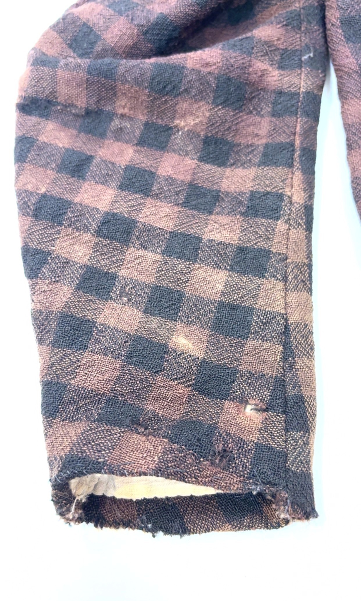 Kjoleliv i svart og brunrutet ull i hjemmevevd toskaft med ermer og bol i samme stoff. Livet er i dag velbrukt, falmet og slitt, med hull på albuene. Sydd for maskin og hånd med panelsøm og bakovertrekte skuldersømmer og sidesømmer. Rund rigning i halsen og buet fremkant. 1,5 cm bred halslinning sydd med maskin og lagt over og festet med faldesting og prikkesting i svart bomullstråd. Tett lukket med 13 par metallhekter med en 1,5 cm bred stolpe som skjuler hektingen. Kantene fremme er først sydd med maskin med brun sytråd og med leggsøm med brun bomullstråd. Livet har et innsnitt som er 3 cm på det bredeste under bysten, sydd med maskin. Smal tosøms krokarm. Livet er helfôret med ubleket bomull i hjemmevevd toskaft og sydd på samtidig som ullstoffet ble sydd sammen med maskin og spilesøm med tykk bomullstråd for hånd. Livet brukes ned i stakken og har hatt en metallkrok midt på bak til å hekte stakken på.