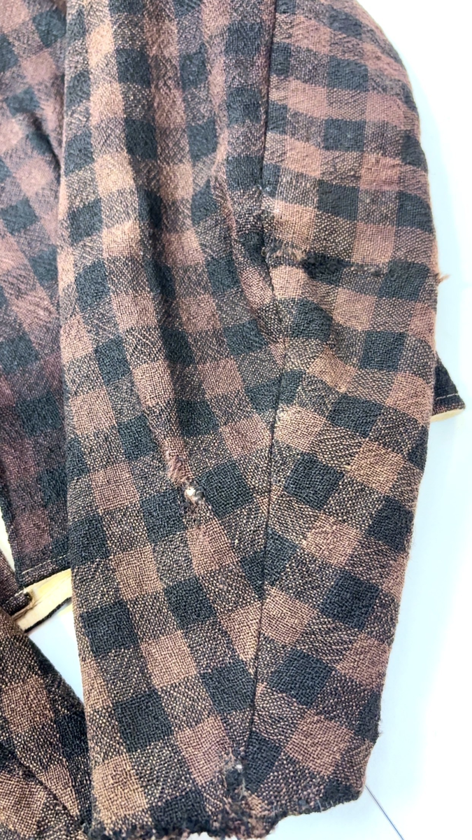 Kjoleliv i svart og brunrutet ull i hjemmevevd toskaft med ermer og bol i samme stoff. Livet er i dag velbrukt, falmet og slitt, med hull på albuene. Sydd for maskin og hånd med panelsøm og bakovertrekte skuldersømmer og sidesømmer. Rund rigning i halsen og buet fremkant. 1,5 cm bred halslinning sydd med maskin og lagt over og festet med faldesting og prikkesting i svart bomullstråd. Tett lukket med 13 par metallhekter med en 1,5 cm bred stolpe som skjuler hektingen. Kantene fremme er først sydd med maskin med brun sytråd og med leggsøm med brun bomullstråd. Livet har et innsnitt som er 3 cm på det bredeste under bysten, sydd med maskin. Smal tosøms krokarm. Livet er helfôret med ubleket bomull i hjemmevevd toskaft og sydd på samtidig som ullstoffet ble sydd sammen med maskin og spilesøm med tykk bomullstråd for hånd. Livet brukes ned i stakken og har hatt en metallkrok midt på bak til å hekte stakken på.