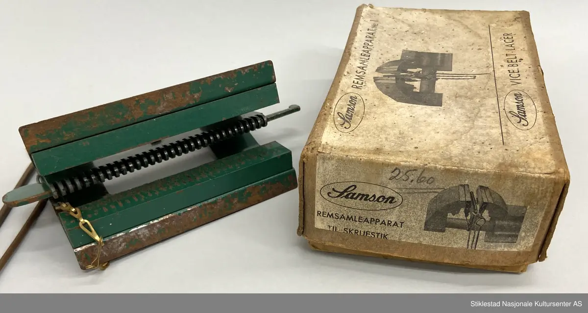 Eske med Samson Reimsamleapparat no 1/Samson Vice belt Lacer. Reimsamleapparat til skrustikke. Apparat i metall, grønnlakkert med prod.merke, uleselig. Mye rust. Fra apparatet henger det to «splinter»  fra en kort kjetting i messing. Esken er i kraftig papp og stiftet sammen. 3 deler. Skrevet med blyant på eska: 25,60 (pris?)