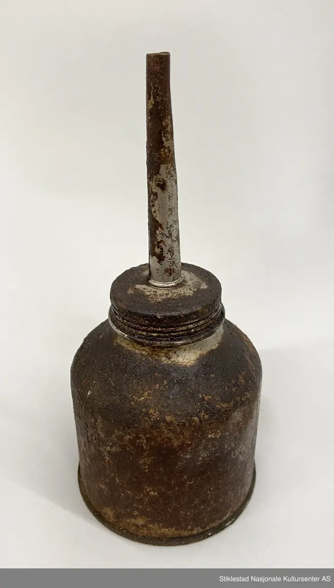 Fabrikkprodusert oljekanne i jernblikk? med rund oljebeholder. Skrukork med tut. En god del oljesøl.