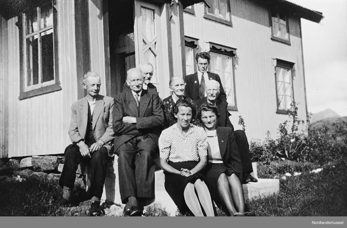 Fem menn og tre kvinner som sitter på en trapp foran et hus.